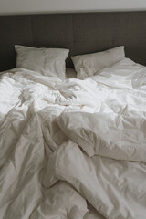 Bedroom concept. Comfortable bed with white crumpled bed linens, pillows. Sunlight shadow reflections. Morning in bed