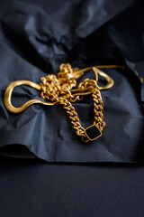 Various gold jewelry. Golden necklace. Long, wide chain on a black background.