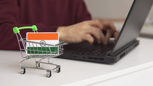 Small shopping cart with Indian Flag on the table. Man using laptop for shopping online.