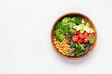 Healthy food in wooden bowl. Chickpeas, lettuce, cherry tomatoes, avocado, broccoli salad. Vegan Budha bowl on light background, top view