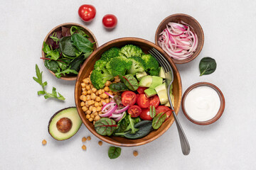 Healthy food in wooden bowl. Chickpeas, lettuce, cherry tomatoes, avocado, broccoli salad. Vegan Budha bowl on light background, top view