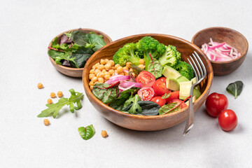 Healthy food in wooden bowl. Chickpeas, lettuce, cherry tomatoes, avocado, broccoli salad. Vegan Budha bowl on light background, top view