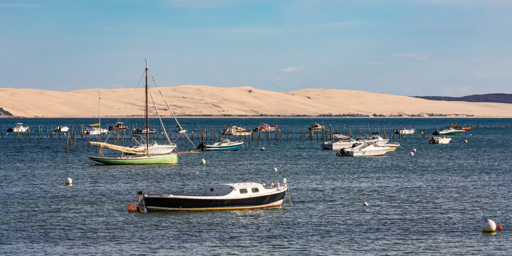 France, Nouvelle-Aquitaine, Lege-Cap-Ferret, Boats floating inArcachonBay with shore of Dune ofPilatin background