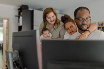Father and daughter using computer with mother holding baby girl in background at home
