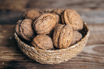 Close-up, whole walnuts in a wicker bowl on a wooden background.