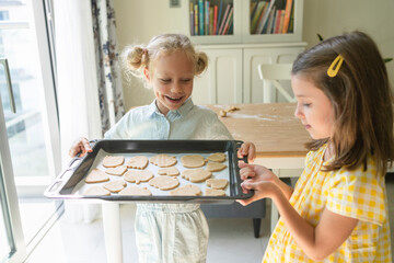Happy girl with friend holding cookie tray at home
