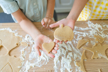 Hand of girl and mother holding cookie dough on table at home