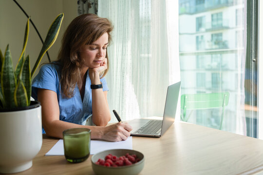 Businesswoman with hand on chin writing on paper at desk in home office