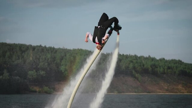 An office clerk flies a flyboard after a day's work. A man performs dangerous and extreme stunts over water