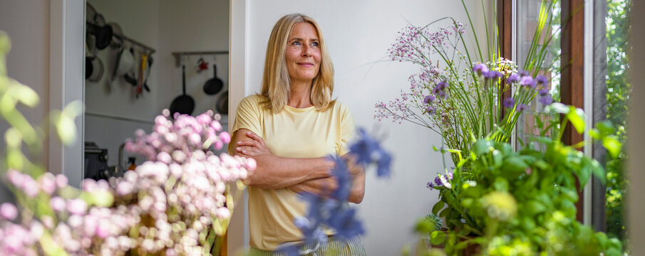 Contemplative mature woman standing with arms crossed at home