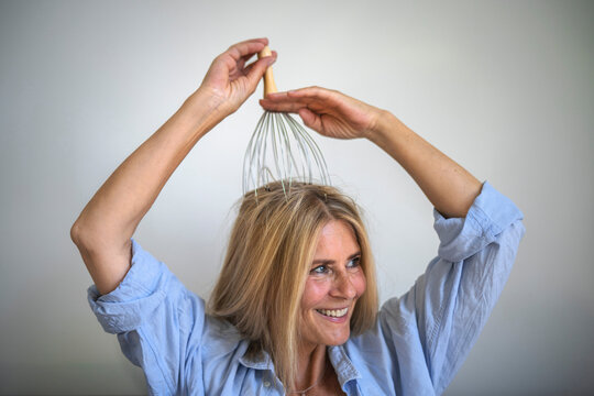 Smiling mature woman head massaging with orgasmatron in front of wall