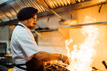 Indian chef flambing food in restaurant kitchen