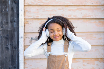 Smiling girl listening to music through headphones in front of wall