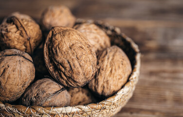 Close-up, whole walnuts in a wicker bowl on a wooden background.