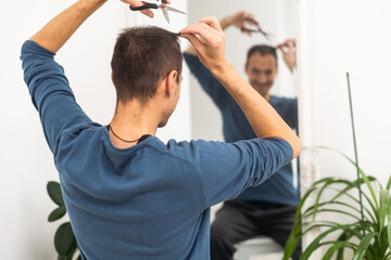 portrait of young man cutting himself hair indoor.