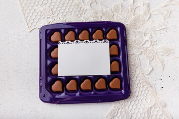 Violet box of heart shaped chocolates, blank postcard on white lace background. Valentines day 14 February sweet present
