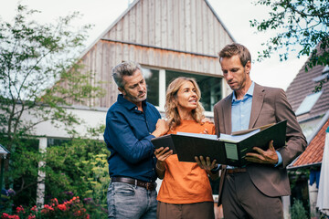 Couple discussing with real estate agent over documents in front of house