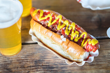 Mustard and ketchup on hot dog with glass of beer at table