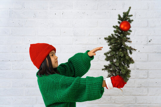 Cute girl holding Christmas tree in front of white brick wall