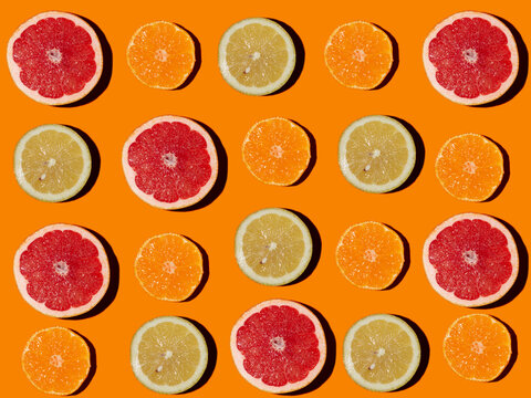 Pattern of halved lemons, grapefruits and tangerines flat laid against orange background