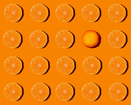 Pattern of halved tangerines flat laid against orange background with single one lying upside down