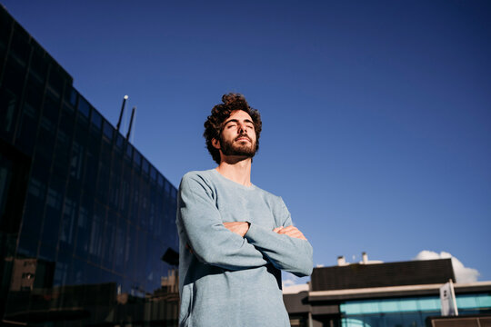 Young Man Standing With Arms Crossed On Sunny Day