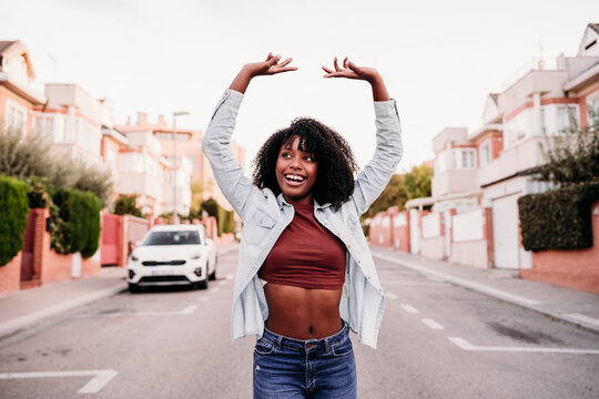 Happy woman with arms raised enjoying dancing on road