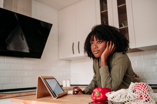 Thoughtful woman leaning on kitchen island at home