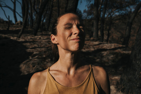 Sad woman standing with eyes closed in burnt forest