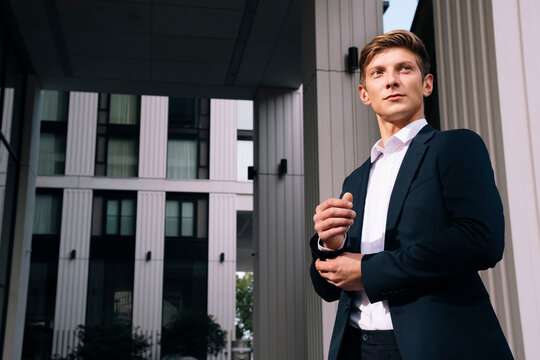 Young businessman adjusting cuff button standing in front of building