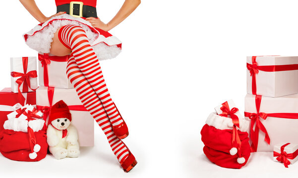 Sexy christmas woman. Beautiful Mrs santa claus legs in striped stockings and high heels next to xmas gifts. Sensual holiday advertise