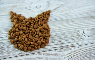Dry pet food on a white, wooden background with a cat head figurine.