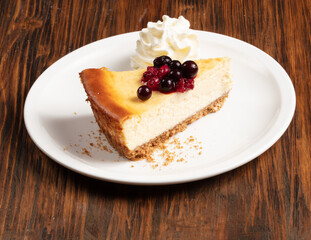 Tarta de queso con frutos del bosque y nata montada sobre mesa de madera. Cheesecake with berries and whipped cream on a wooden table.