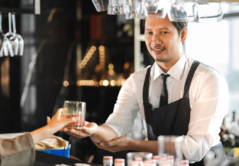 Barkeeper serving alcohol drink to a man at pub. Smiling male bartender holding glass of cocktail...