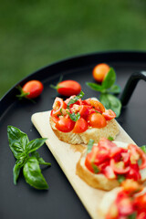 Italian bruschetta with fresh red tomatoes and basil herbs on a wooden board outdoor on the yard, backyard at home, sunlight. Classic Italy food, antipasto