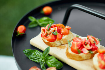 Italian bruschetta with fresh red tomatoes and basil herbs on a wooden board outdoor on the yard,...