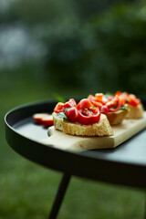 Italian bruschetta with fresh red tomatoes and basil herbs on a wooden board outdoor on the yard, backyard at home, sunlight. Classic Italy food, antipasto