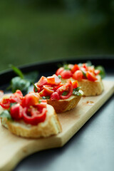 Italian bruschetta with fresh red tomatoes and basil herbs on a wooden board outdoor on the yard, backyard at home, sunlight. Classic Italy food, antipasto