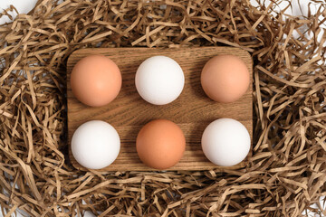 White and brown eggs on wooden tray in strip paper filling of stylized nest close view from above. Ingredients of healthy nutrition and diet, flat lay.