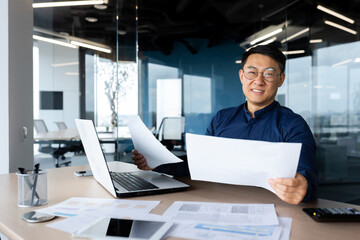 Plakat Portrait successful satisfied asian financier accountant, man in shirt and glasses working inside office using calculator and laptop for accounts and financial documents reports, looking at camera.