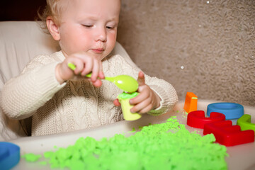 baby holds mold for playing with sand at home. Educational toys for children up to year. girl plays with kinetic sand. child builds shepherds in form of letters of sand. Early development of children.
