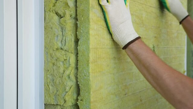 Builder insulates the external walls with mineral sheet insulation in protective gloves. Thermal insulation work, house renovation.
