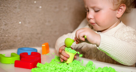 baby holds mold for playing with sand at home. Educational toys for children up to year. girl plays with kinetic sand. child builds shepherds in form of letters of sand. Early development of children.