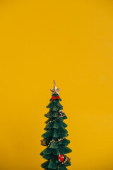 A candle in the shape of a Christmas tree with gifts on branches on a yellow background. Minimalism, still life.