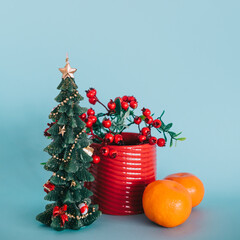 Christmas tree with a branch of winter berries in a red mug and two tangerines on a blue background - 549671085