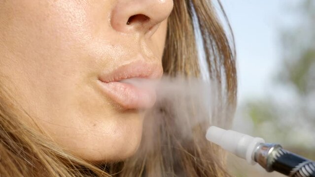 closeup of woman's lips exhaling smoke from electronic cigarette