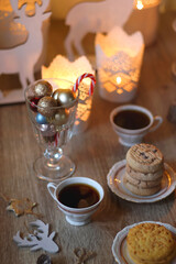 Two types of cookies, cups of tea or coffee, various Christmas decorations and lit candles. Cozy Christmas atmosphere at home. Selective focus.
