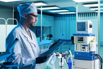 Naklejka premium Man doctor. Employee of clinic holds test tube with blood. Nurse in anesthesiologists office. Medical lab worker. Doctor stands in interior of hospital. Doctor man near anesthesia equipment
