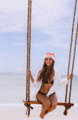 Beautiful young female sitting on the swing on sea shore enjoy christmas time at vacation