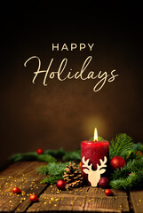 Grußkarte, Weihnachtskarte mit englischem Text Happy Holidays. Dekoration mit roter Kerze, Tannenzweigen, Zapfen, Kugeln und Rentier auf Holz. Hochformat. - 549674220